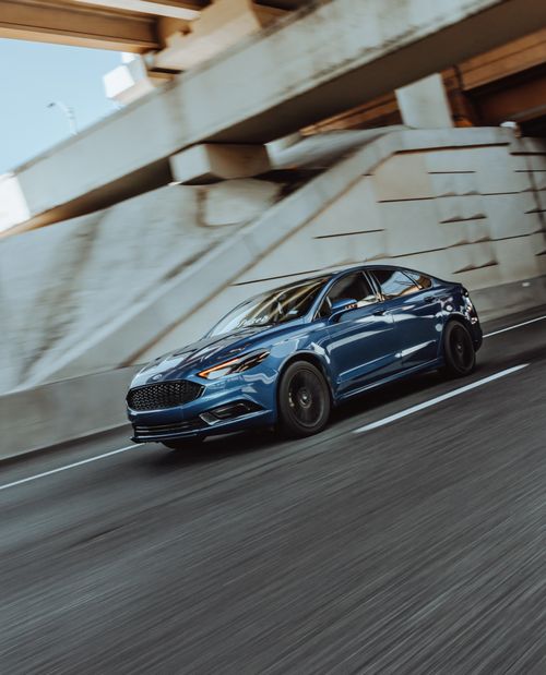 Free Blue car speeding on a city highway under an overpass, showcasing modern design and speed. Stock Photo