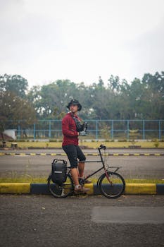 Asian man with hat resting on a foldable bicycle outdoors.