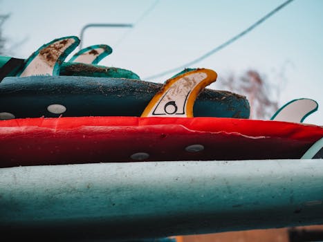 A detailed close-up of colorful surfboards stacked with visible dirt and fins, capturing a raw beach vibe.