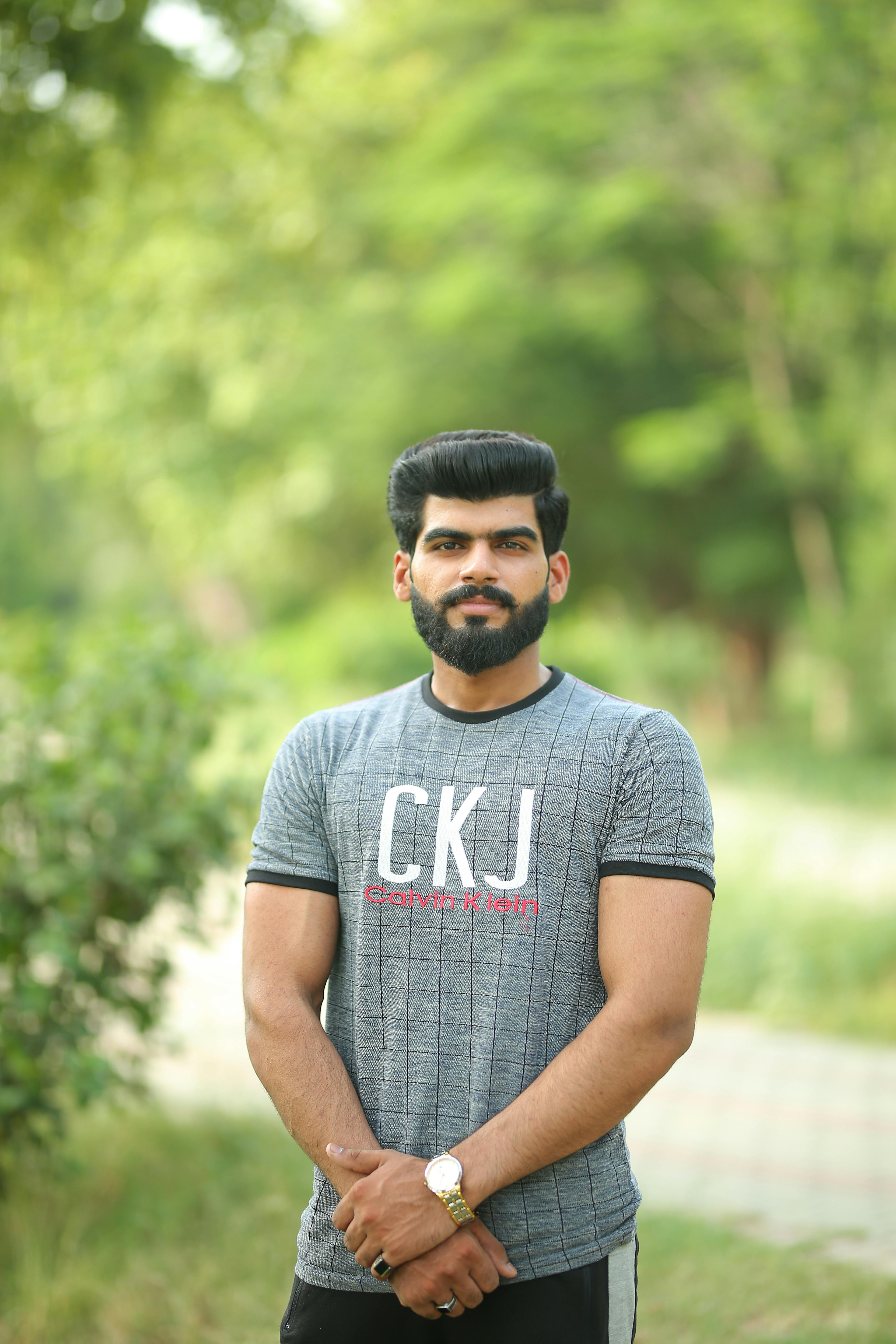 A confident, bearded man in casual clothing posing in a lush green park in Lahore, Pakistan.