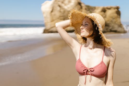 Woman in a Bikini and a Straw Hat Walking on a Beach 