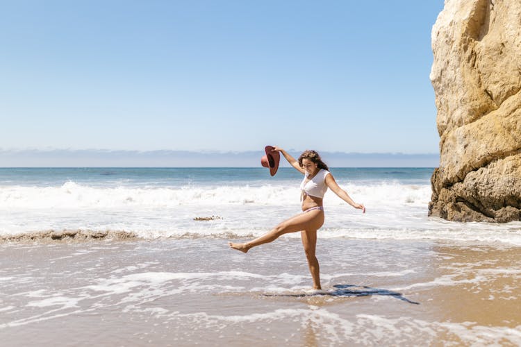 A Woman In White Bikini Kicking Water On Shore