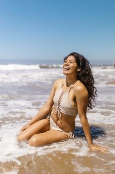 A woman in a bikini laughing and enjoying the beach waves during summer.