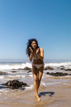 Woman in a swimsuit enjoying a sunny beach with waves in the background.