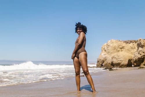 Free A joyful woman in swimwear enjoying a sunny day on a sandy beach by the ocean. Stock Photo