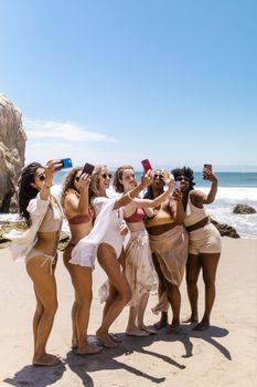 A diverse group of women in swimwear taking a selfie at a sunny beach.