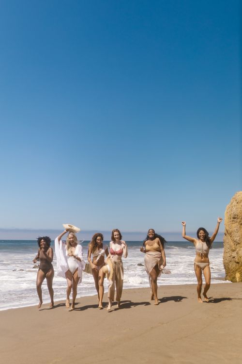 Free Six women in swimsuits enjoying a vibrant summer day at the beach with blue skies. Stock Photo