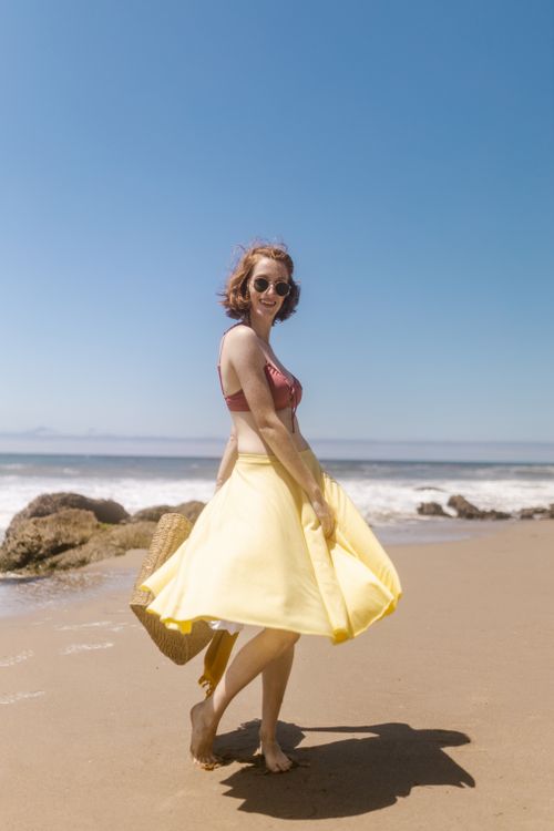Free A joyful woman in a red bikini top and yellow skirt, barefoot on a sunny beach. Stock Photo