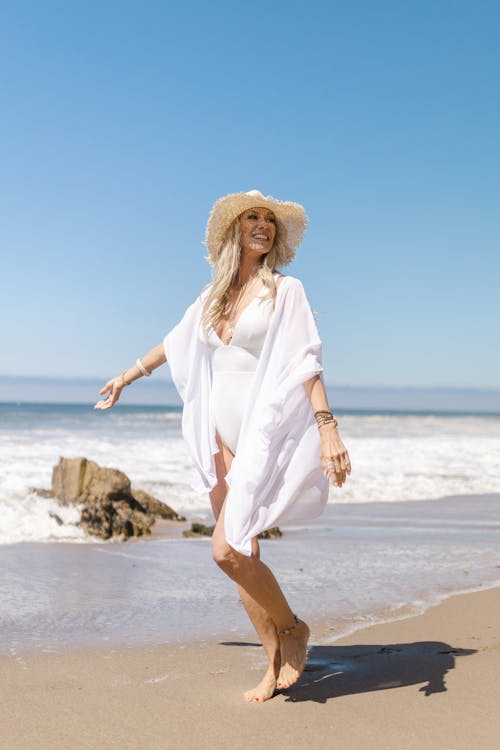 Free A Woman in White Bikini Walking on the Beach Stock Photo