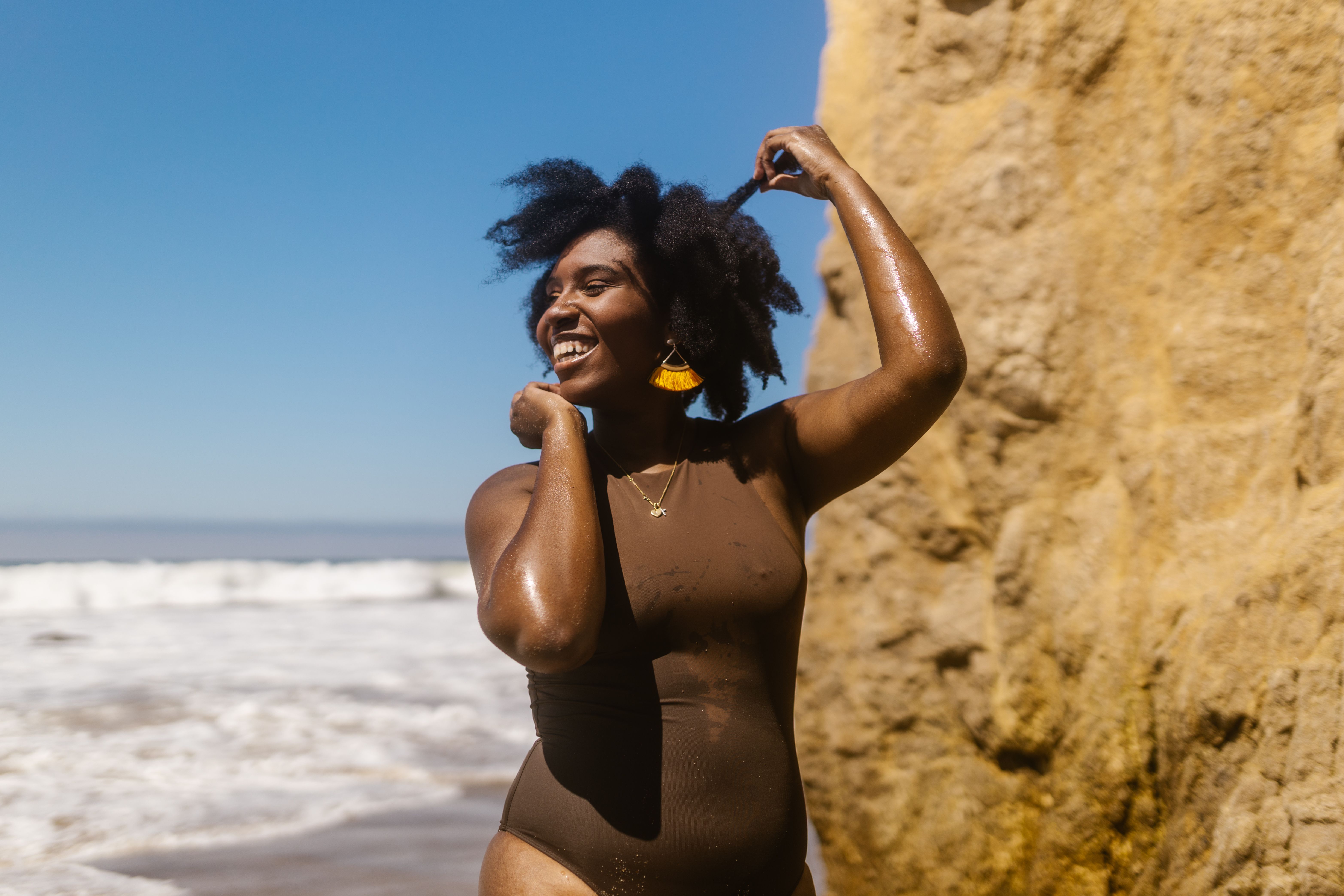 Smiling woman in a swimsuit enjoying a sunny day at the beach, capturing a moment of happiness and freedom.