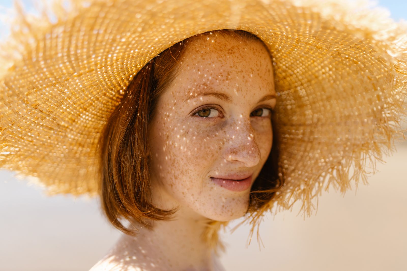 Woman wearing a woven straw hat with warm sunlight filtering across her freckled face.