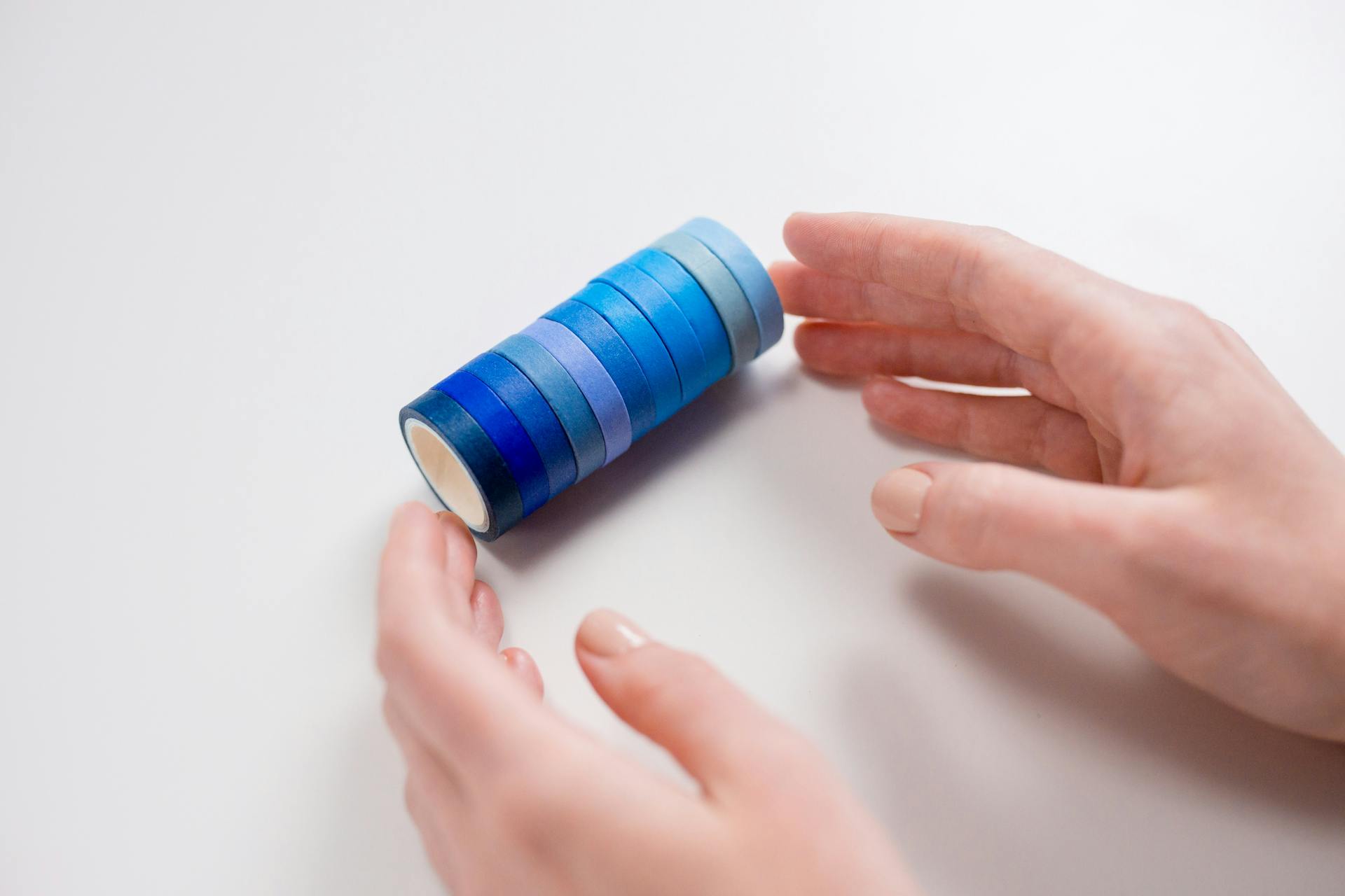 Close-up of hands arranging blue washi tape rolls on a white background, emphasizing creativity.