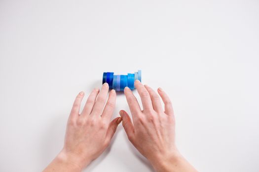 Hands reaching for a stack of blue gradient tapes on a white background, showing colors and minimalistic style.