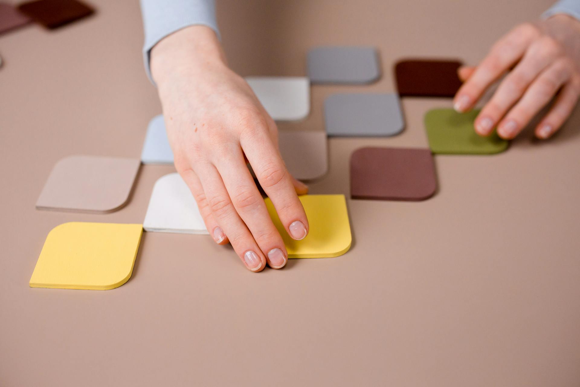 Close-up of hands arranging pastel and vibrant paper squares on a flat surface, exploring creativity.