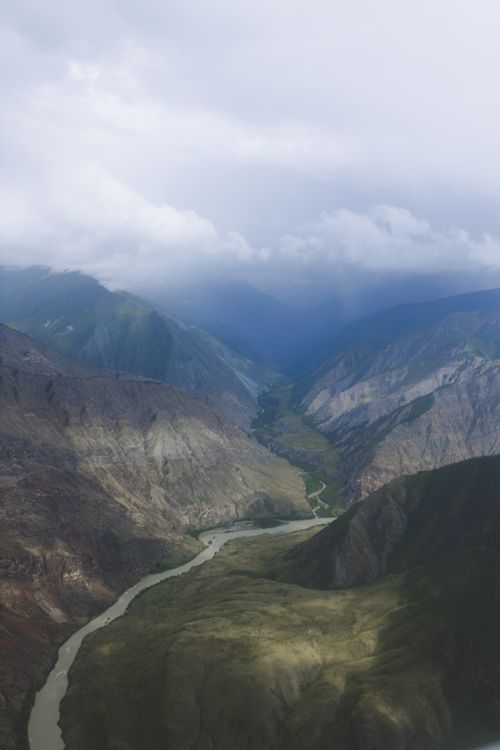 Free A breathtaking aerial view of a dramatic mountain landscape with a winding river and cloudy sky. Stock Photo