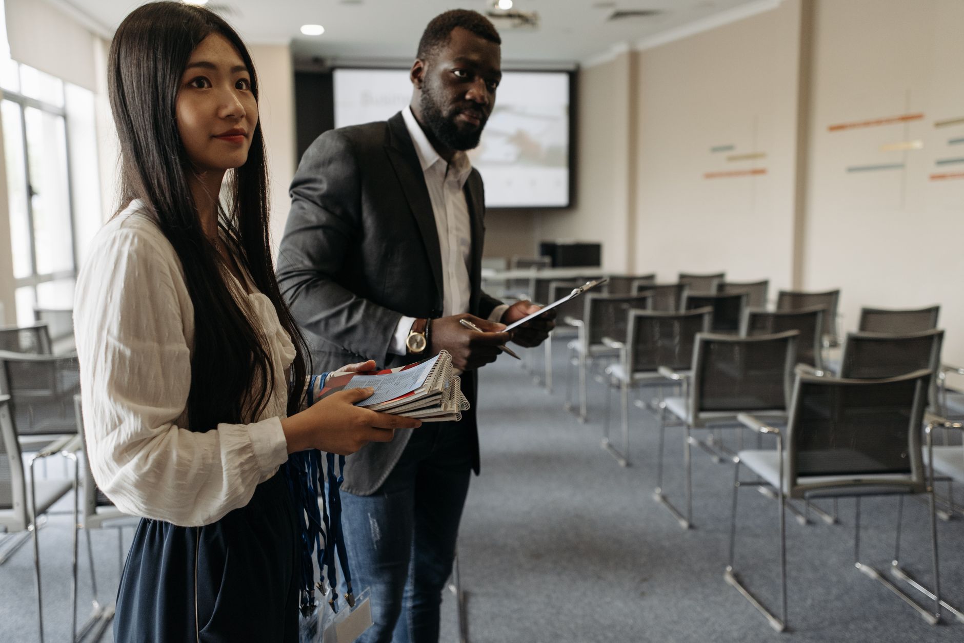Two professionals hold notepads in a modern conference room setting.