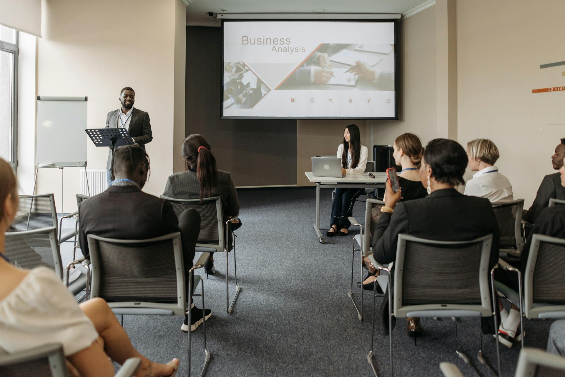 A Man Speaking in Front of the People Sitting Inside the Conference Room