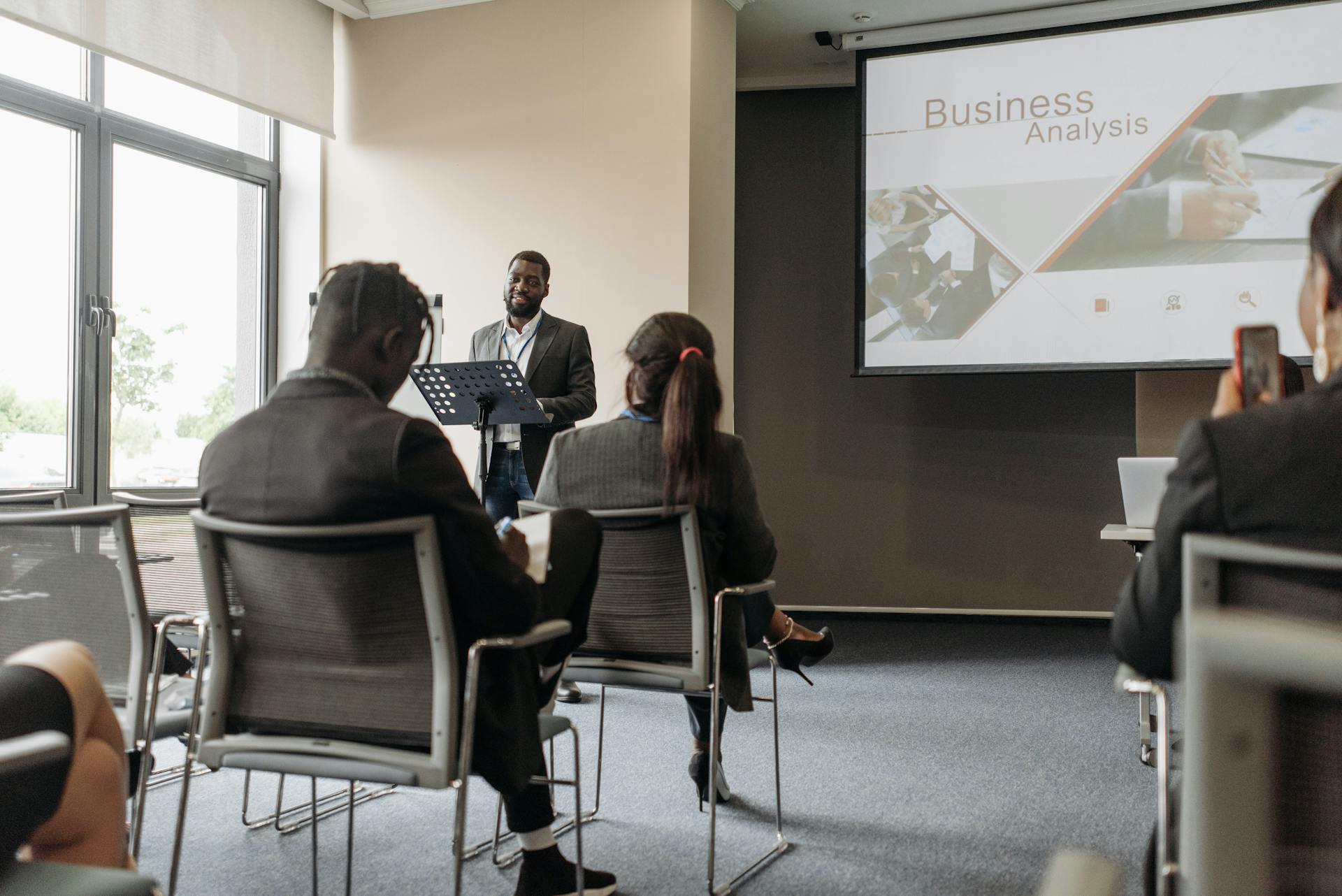 A business professional delivering a presentation in a conference room with diverse attendees.