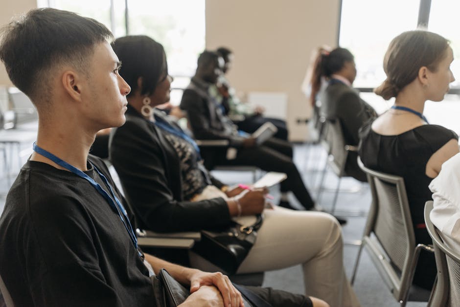 A diverse group of adults attentively listening at a conference setting, featuring name tags and formal attire.
