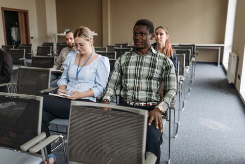 Free A diverse group of adults sitting in a seminar room attentively listening to a presentation. Stock Photo