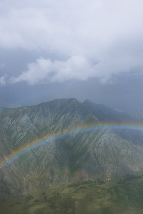 A Beautiful Rainbow Near Green Mountains Under White Clouds