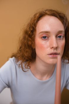 Close-up portrait of a woman with red curly hair holding a candle in a studio.