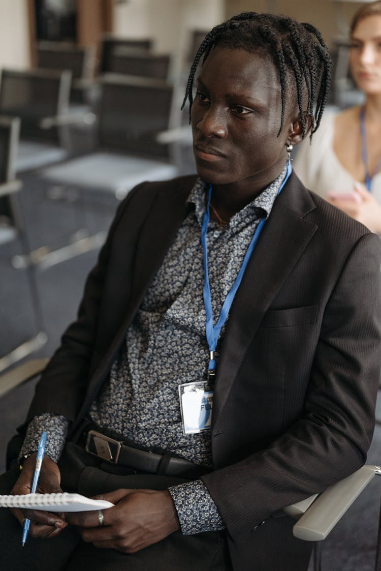 Man In Black Suit Wearing Lanyard While Sitting On A Chair