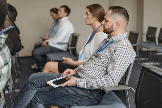 Adults attending a business seminar, attentively listening with notebooks and smartphones.