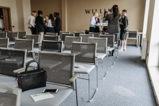 An empty conference room with chairs and a group of people gathered at the back.