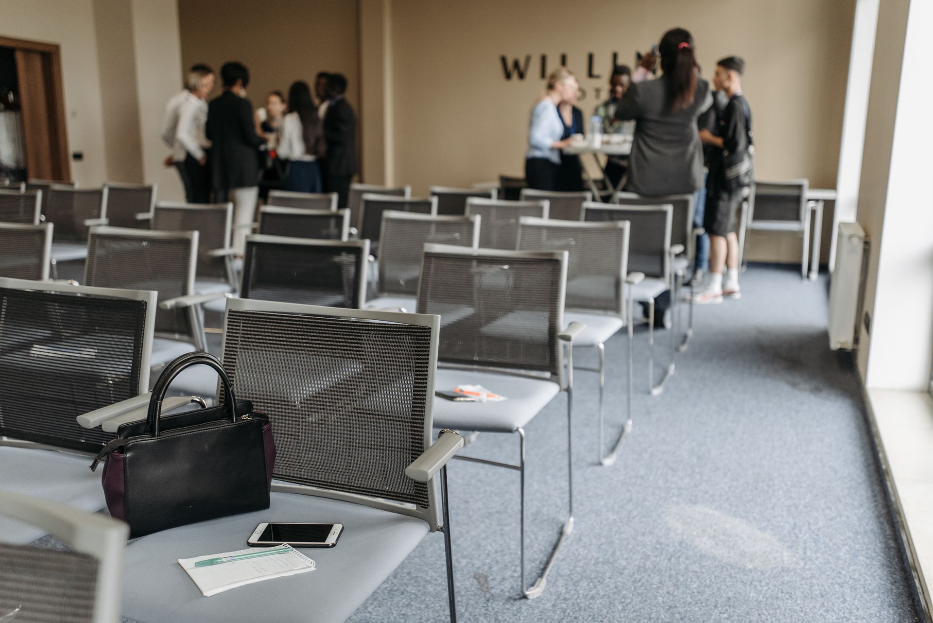 An empty conference room with chairs and a group of people gathered at the back.