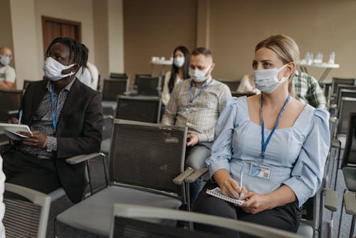Group of People Wearing Face Masks and Badges Taking Notes in a Conference Room