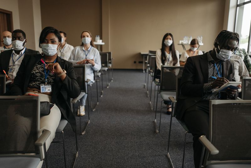 Business professionals at a socially distanced conference meeting during the pandemic, all wearing masks.