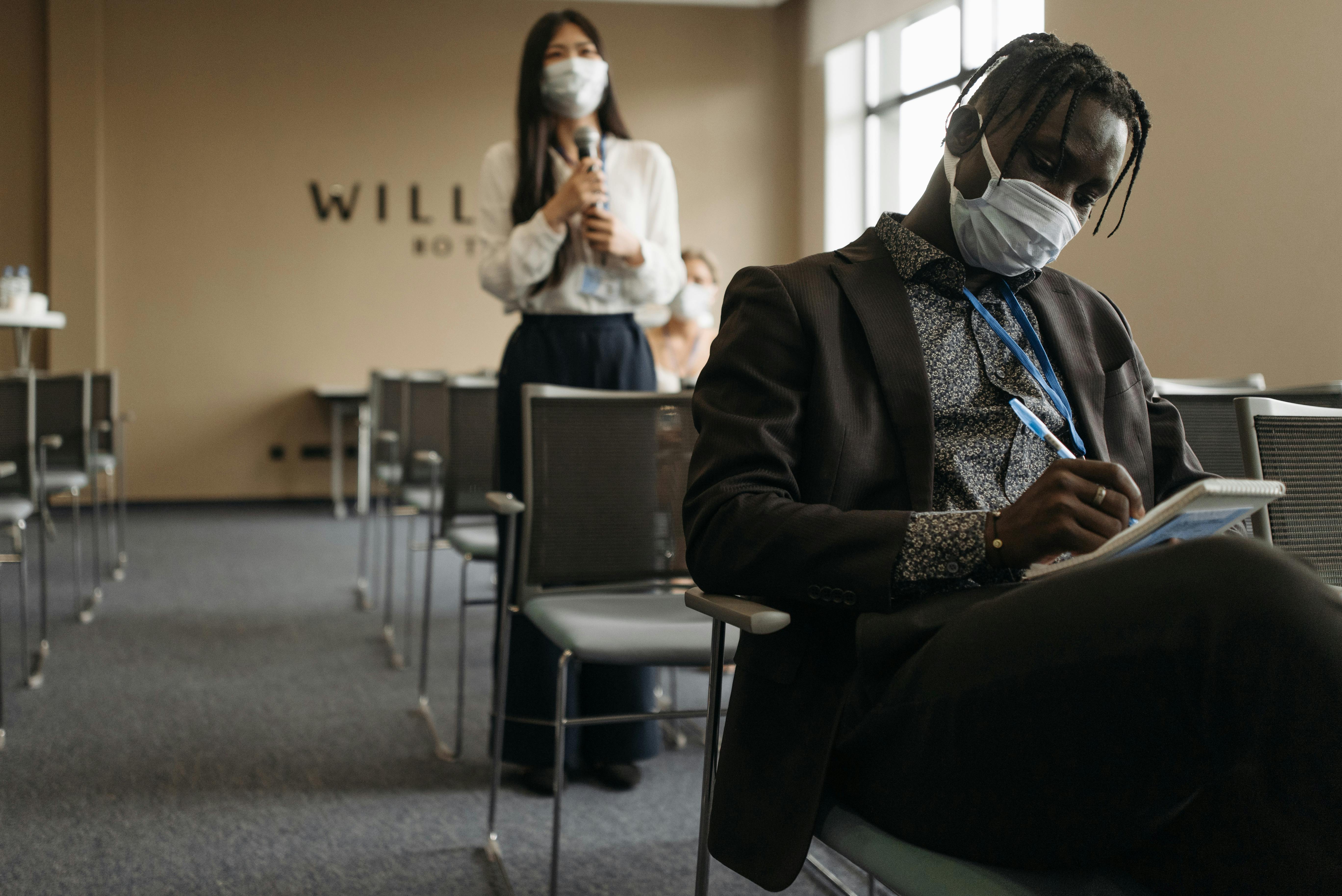 Professional conference room setting with participants wearing masks, engaging in a meeting.