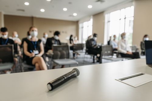 Free A business conference room setting with masked participants and a microphone in the foreground. Stock Photo