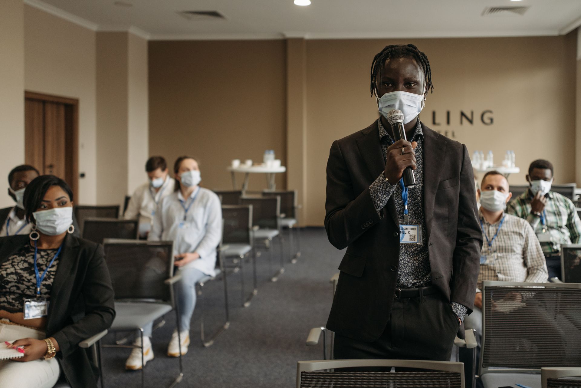 Man in Blazer Suit and Face Mask Holding a Microphone in a Meeting Room