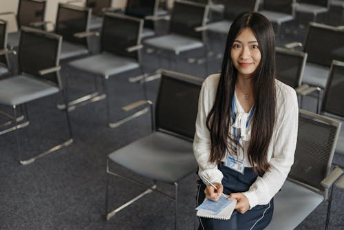 Woman in White Top Holding Pen and Spiral Notebook