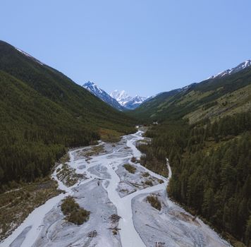 Stunning aerial view of a river valley in the Altai Mountains, Russia, surrounded by lush greenery and majestic peaks.