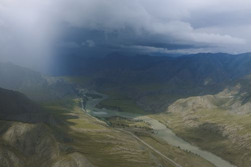 Free Aerial view of a river winding through dramatic mountain landscape under stormy clouds. Stock Photo