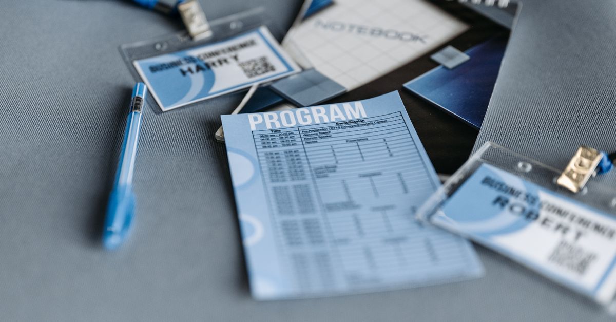 Close-up of conference materials including name tags, program, and pen on a gray surface.