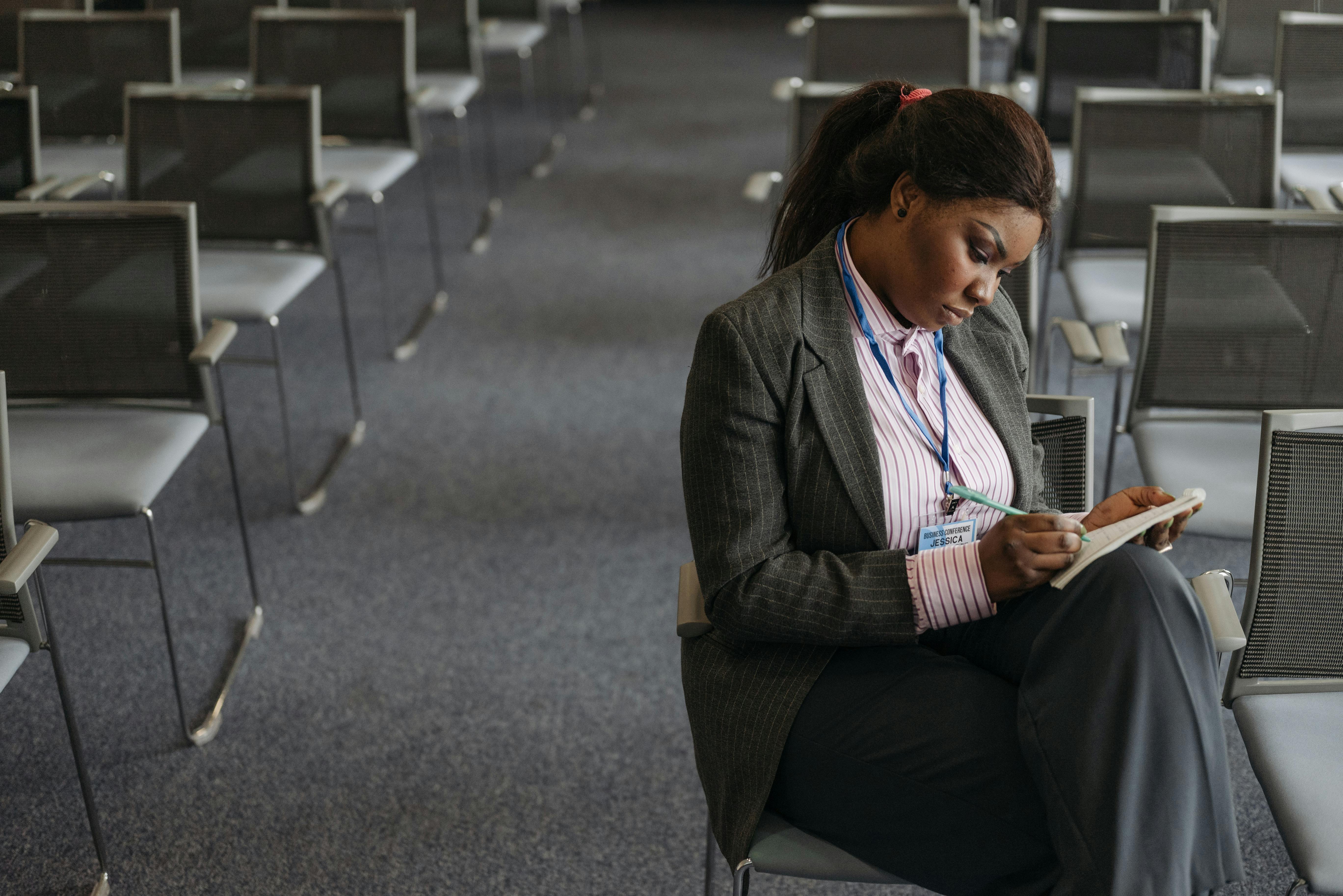 Free A Woman in Black Blazer Writing while Sitting on a Chair Stock Photo