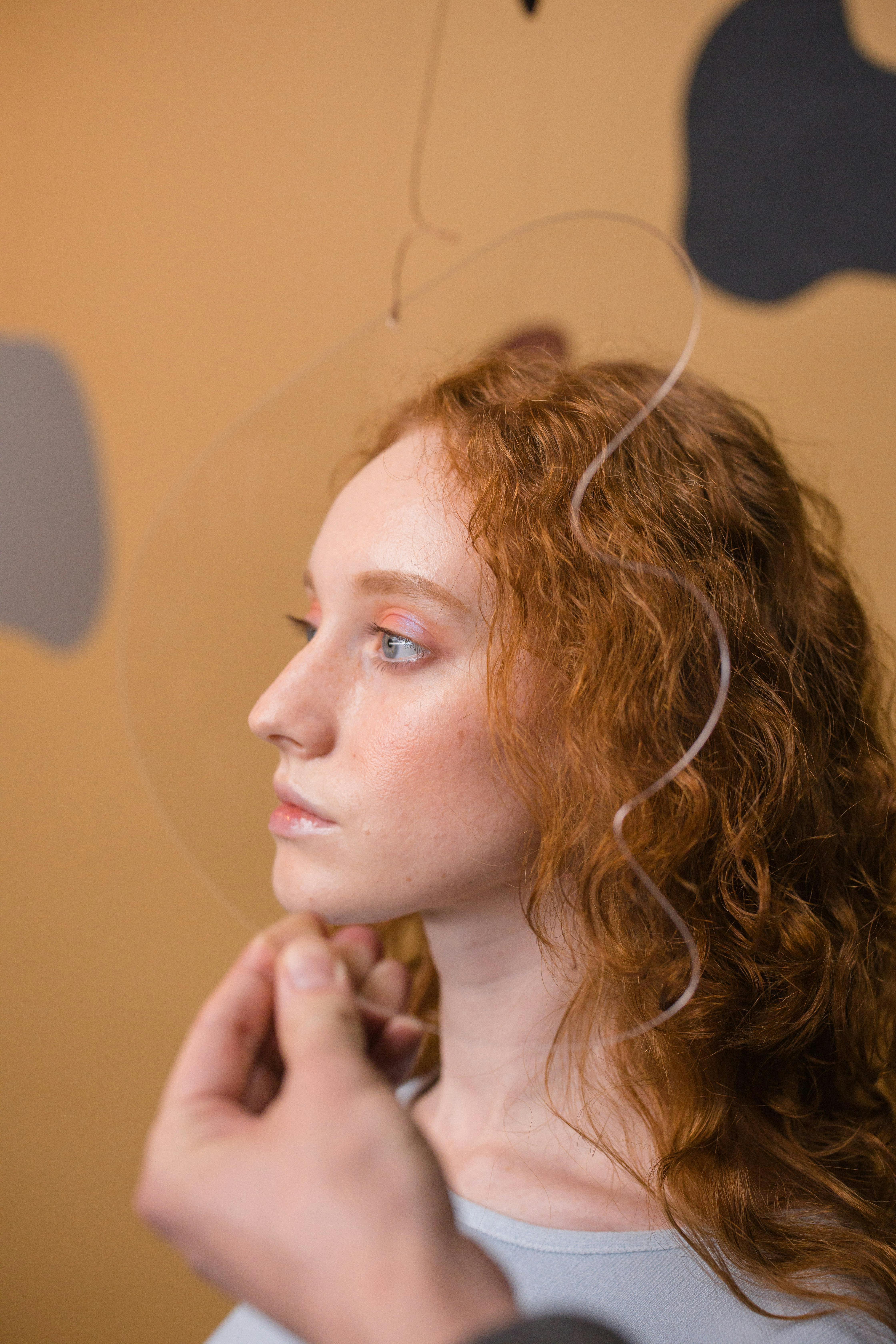 Profile shot of a woman with curly red hair holding a transparent object, studio setting.