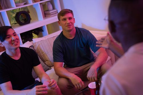 Free Three friends chat and relax on a sofa in a warmly lit living room. Stock Photo