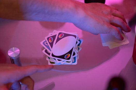 Close-up of hands engaged in a game of cards with vibrant lighting on a table.