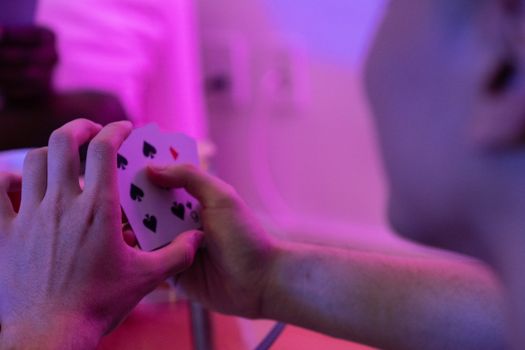 Atmospheric shot of hands holding playing cards with vibrant neon lighting creating a dynamic focus.