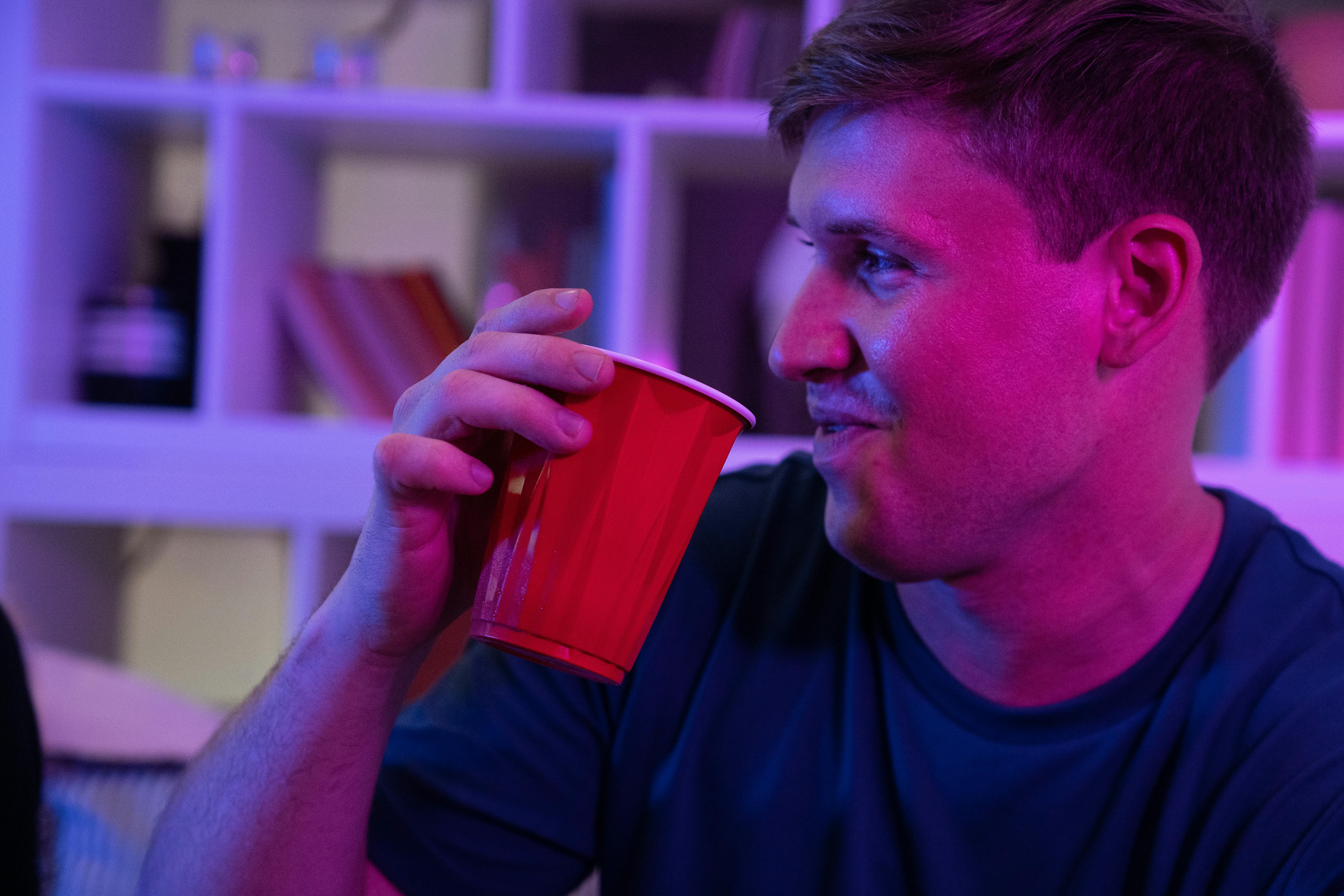 A young man smiling while holding a red cup at an indoor party.
