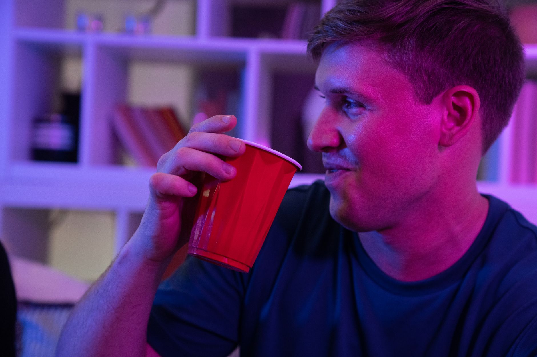 A young man smiling while holding a red cup at an indoor party.