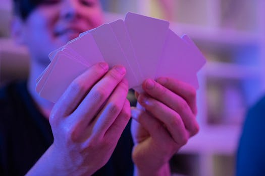 Close-up of hands holding blank cards with colorful lighting indoors, emphasizing card games or magic tricks.