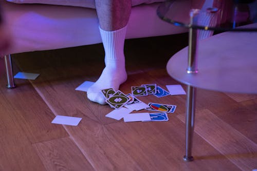 A Person Stepping on a Wooden Floor Near the Scattered Uno Cards