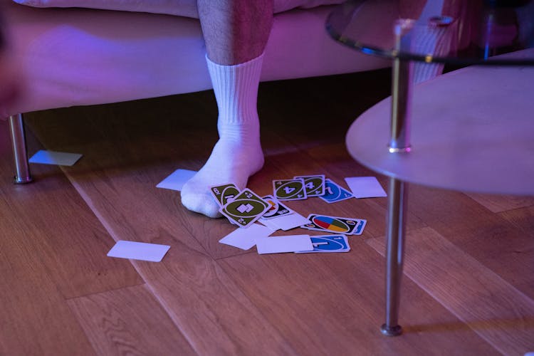 A Person Stepping On A Wooden Floor Near The Scattered Uno Cards