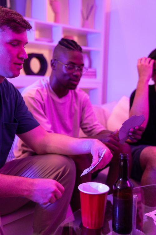 Free Young adults playing cards on a cozy night with drinks and snacks. Stock Photo